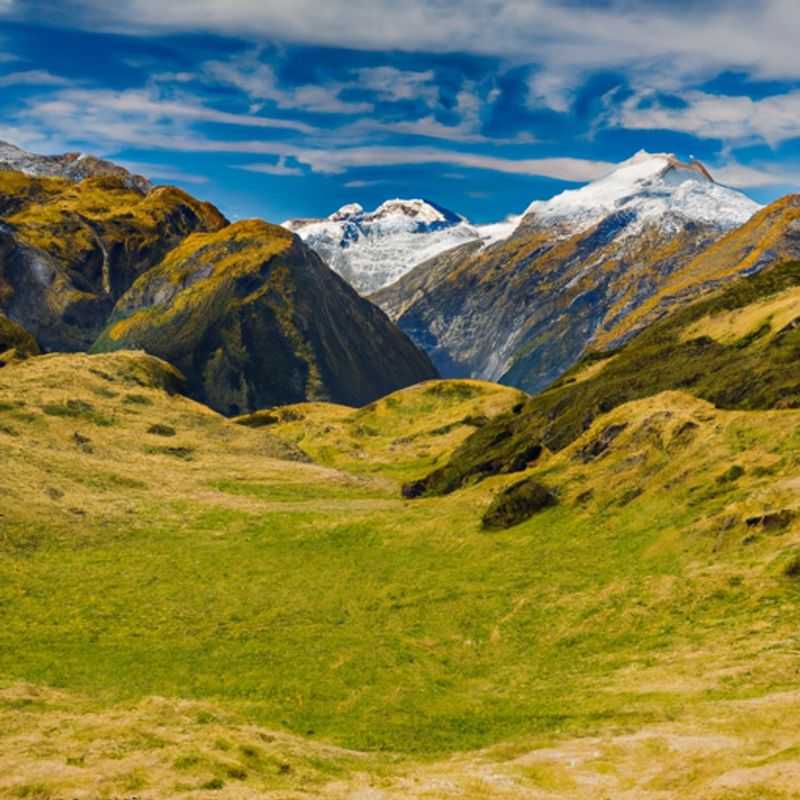 A lone traveler stands at Cascade Saddle, New Zealand, marveling at the breathtaking winter wonderland that unfolds before them. Snow-capped mountains rise majestically, casting long shadows across the icy landscape, while the crisp winter air invigorates the soul.